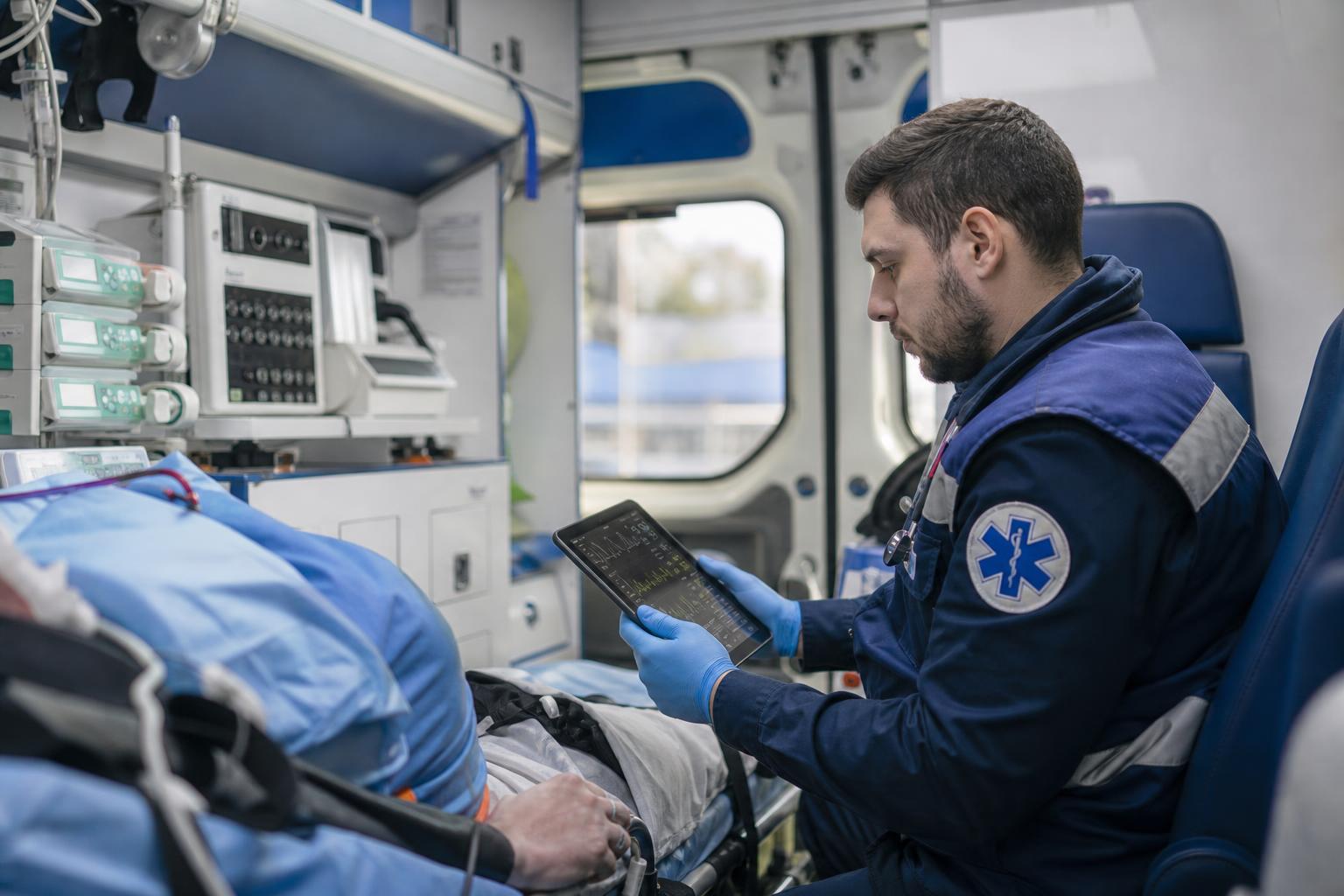 Врач скорой помощи использует цифровой планшет для мониторинга показателей пациента во время транспортировки